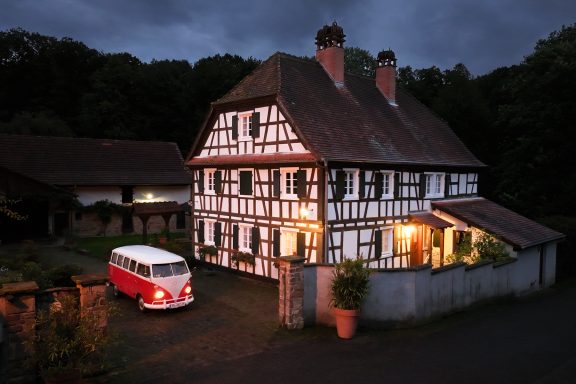 Rotweißer VW Bulli vor einem Fachwerkhaus in der Nacht