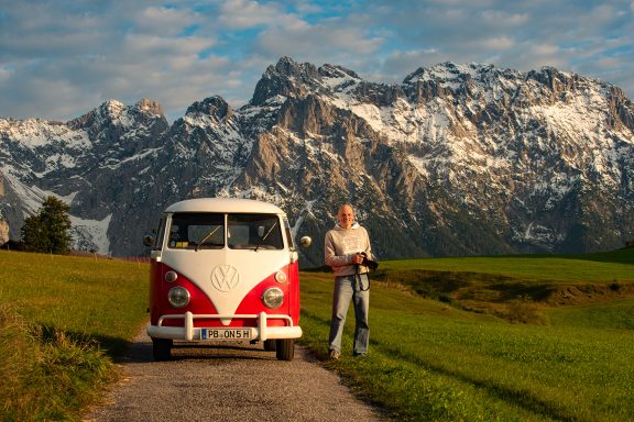 Rotweißer VW Bulli mit dem Fotograf Peter Gebhard davor und im Hintergrund sehr hohe Berge